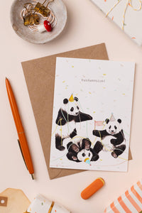 Greeting card with panda illustrations on a beige surface with stationery items.