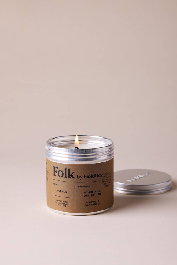 Candle in a 'Folk' by Field Day container with a lit wick on a beige background