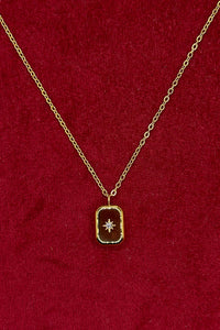 A gold chain necklace with a small rectangular pendant featuring a central star motif, displayed on a textured red velvet background.