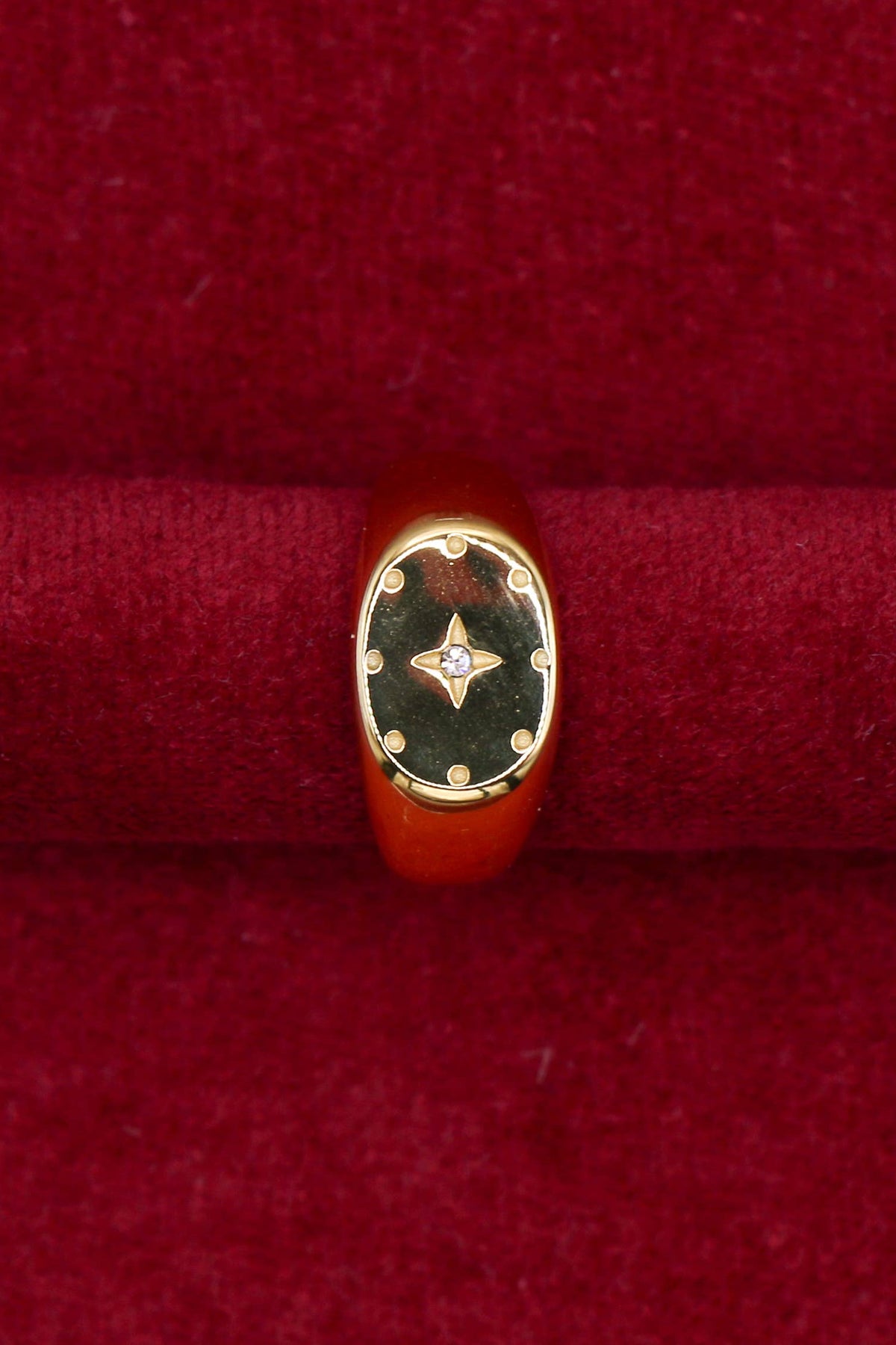 A gold signet ring with a black enamel face and a small central diamond, displayed on a red velvet ring box.