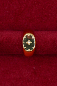 A gold signet ring with a black enamel face and a small central diamond, displayed on a red velvet ring box.