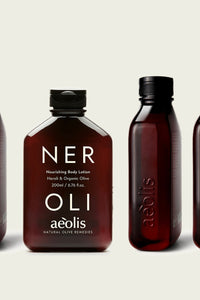 Four amber-brown bottles of aloe vera body lotions from the brand aéolis, arranged in a row against a light beige background. The center bottle is fully visible and labeled 'NER OLI Nourishing Body Lotion', while the bottles on the sides are partially cropped.
