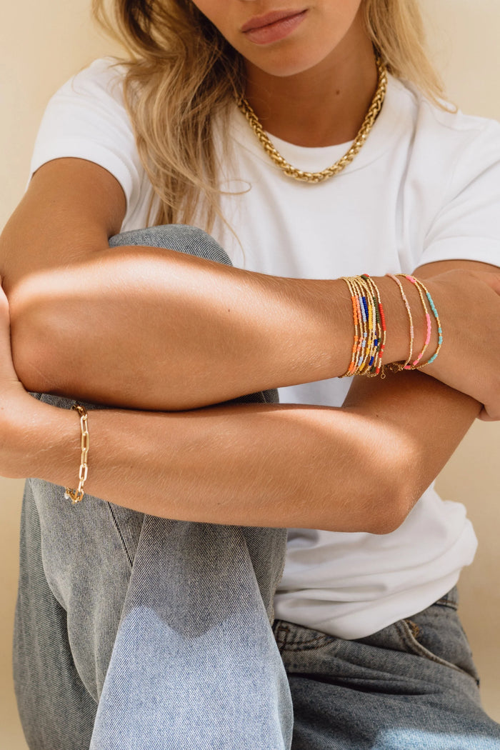 Person wearing a white t-shirt, gold necklace, and colorful bracelets on a beige background