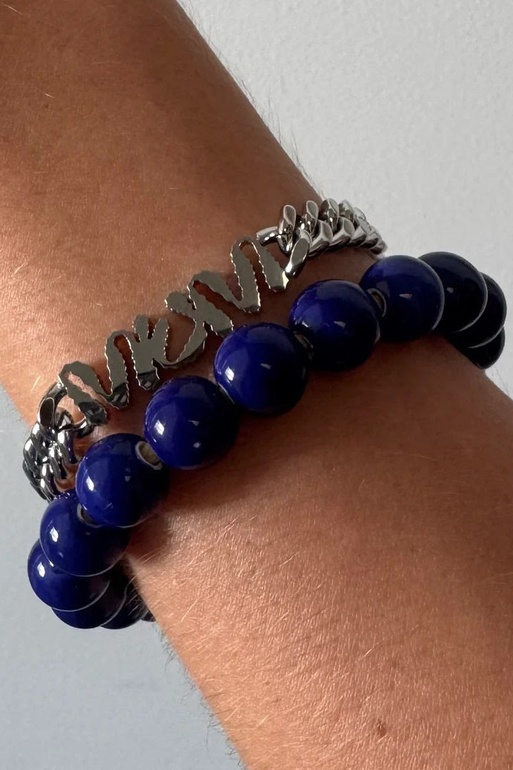 Two bracelets on a wrist, one with blue beads and the other with silver chain design, against a neutral background.