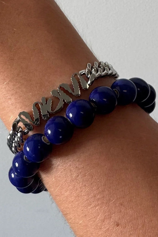 Two bracelets on a wrist, one with blue beads and the other with silver chain design, against a neutral background.