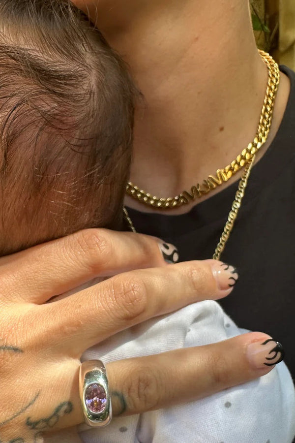 Person holding a baby close, wearing a gold chain and ring.