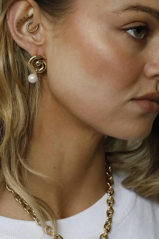 Woman wearing a gold necklace and earrings with a plain background