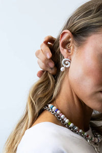 Woman wearing a colorful beaded necklace and white earrings against a light background