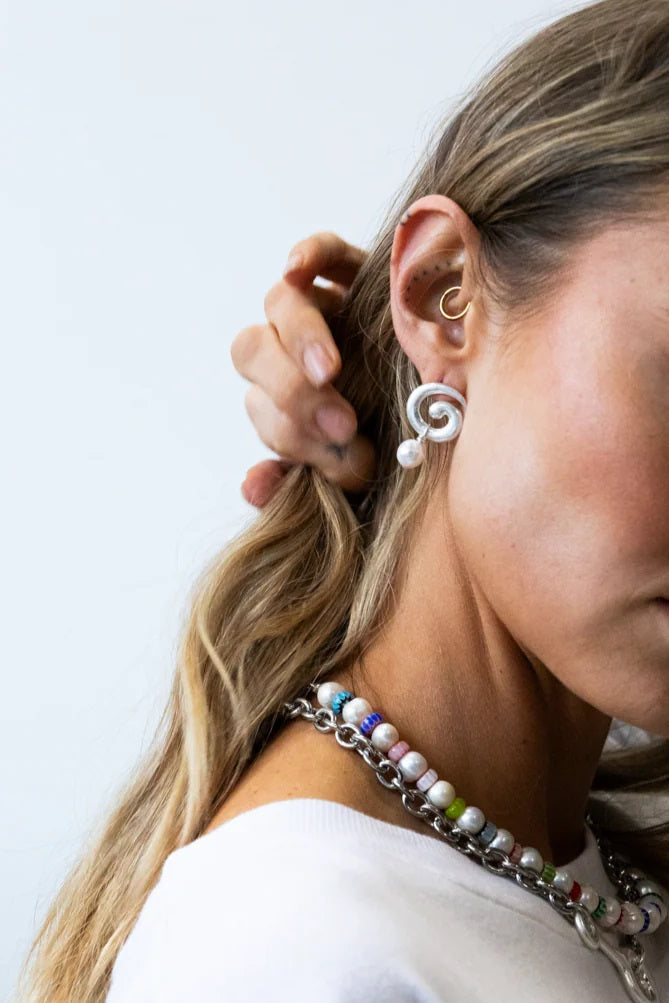Woman wearing a colorful beaded necklace and white earrings against a light background