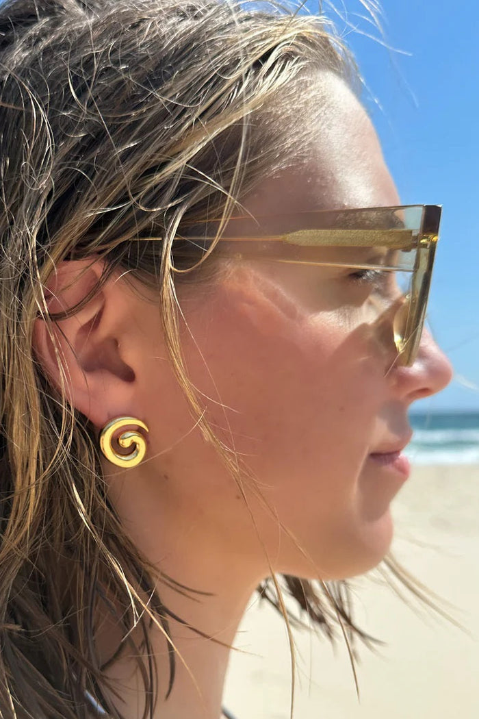 Woman wearing gold sunglasses and earrings on a beach