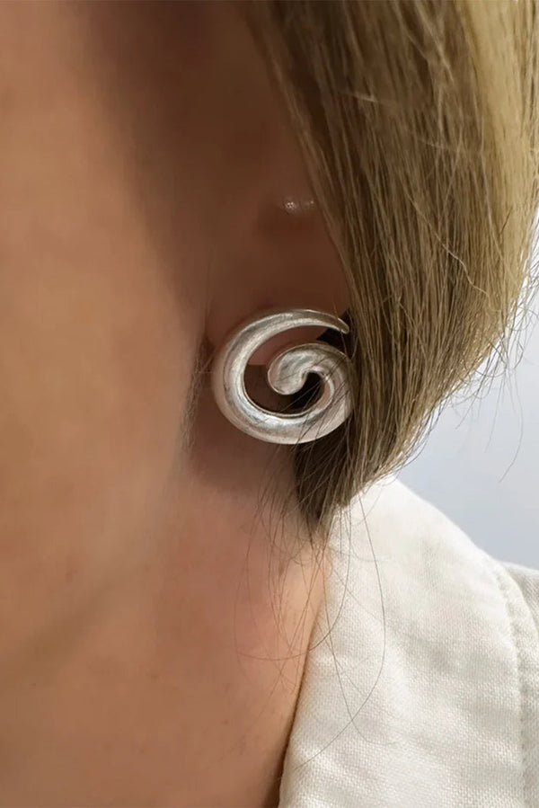 Silver spiral earring worn by a person with a neutral background