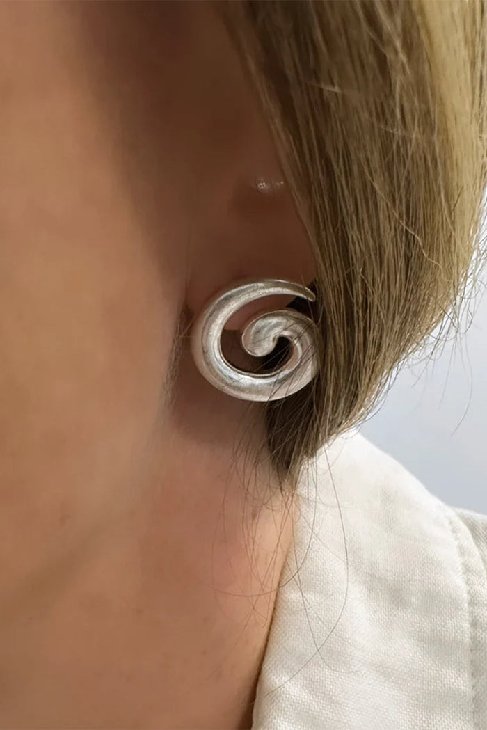 Silver spiral earring worn by a person with a neutral background