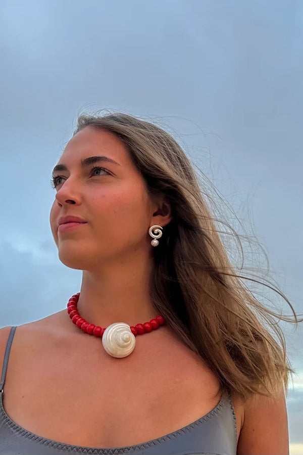 Woman wearing a red necklace with a shell pendant against a cloudy sky
