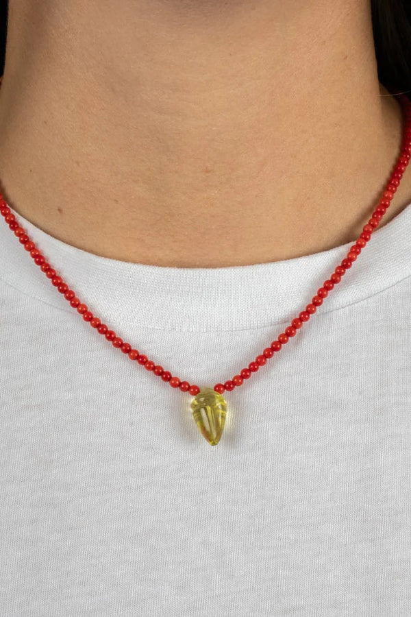 Red beaded necklace with a gold pendant worn by a person on a white background