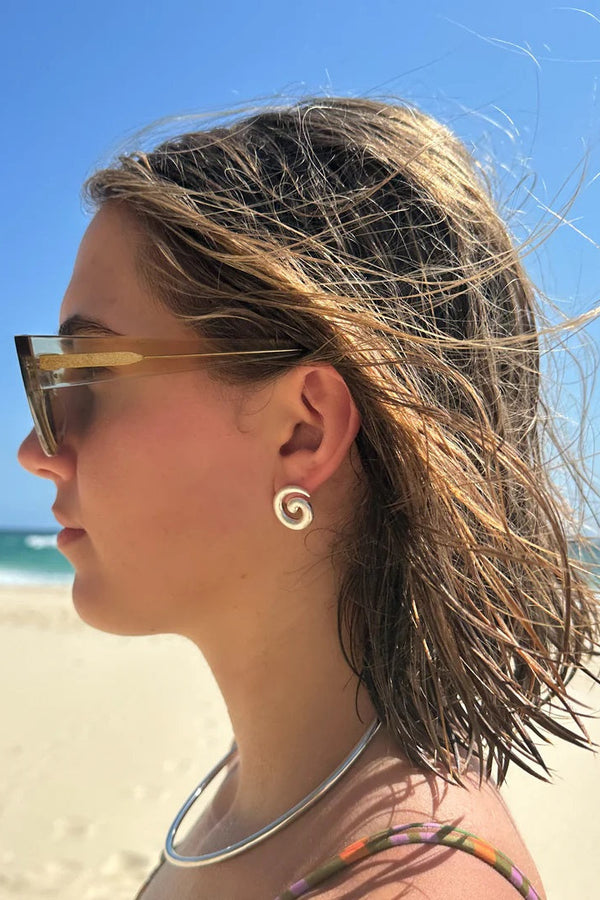 Woman on a beach wearing sunglasses and a necklace with a clear blue sky and ocean in the background