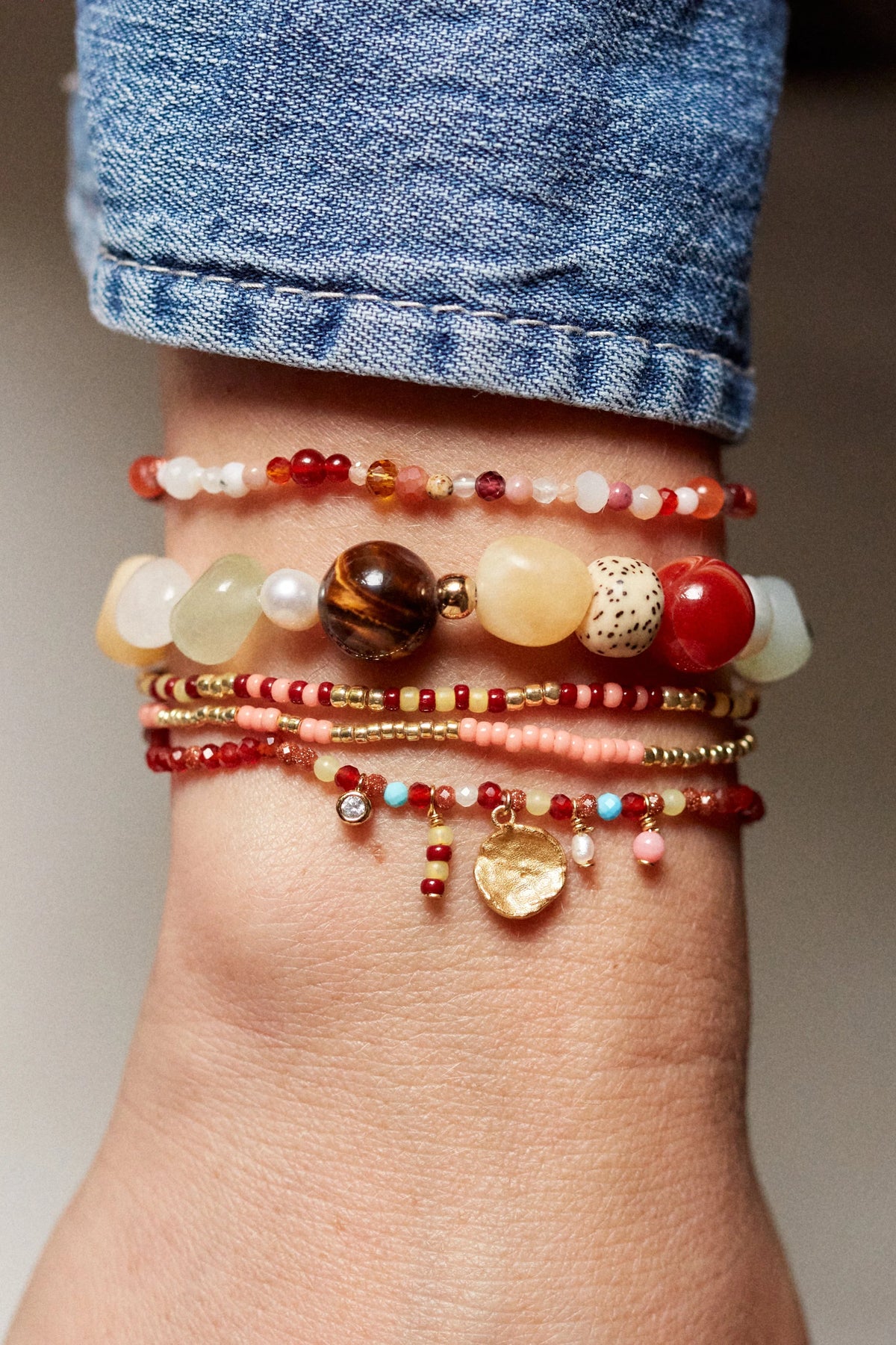 Multiple beaded bracelets on a wrist with a denim sleeve.