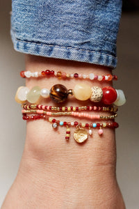 Multiple beaded bracelets on a wrist with a denim sleeve.