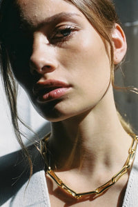 Close-up of a woman wearing a gold necklace with a blurred background
