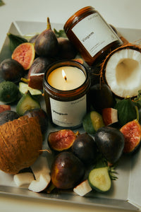 Vigem candle and jars surrounded by figs and coconuts on a white surface
