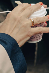 A close-up of a person's hands holding a takeaway coffee cup with a lid and straw. The cup is branded 'GROUND E' with a pink smiley face pattern.