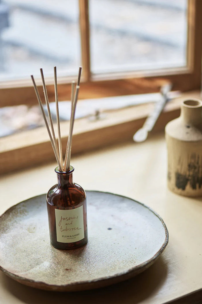 Diffuser bottle with sticks on a ceramic plate by a window