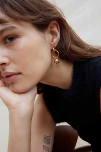 Close-up of a woman wearing gold hoop earrings with a neutral background