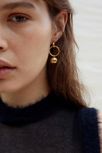 Close-up of a person wearing gold hoop earrings with a neutral background