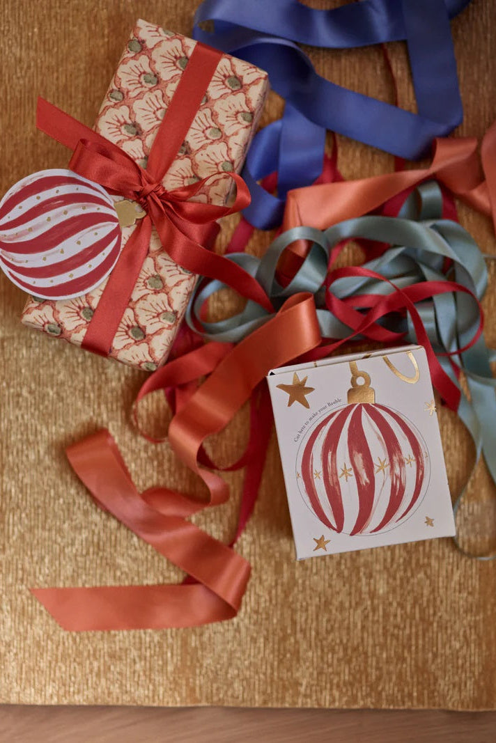 Gift box with red ribbon, Christmas ornament, and card on a wooden surface