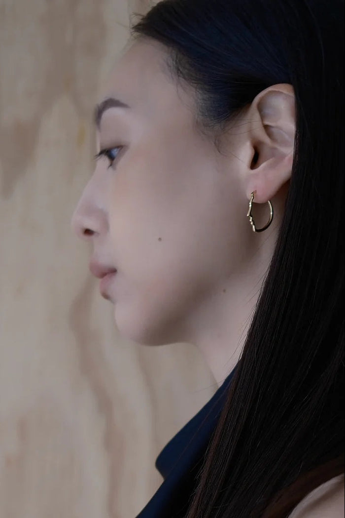 Close-up of a person wearing a gold hoop earring against a wooden background