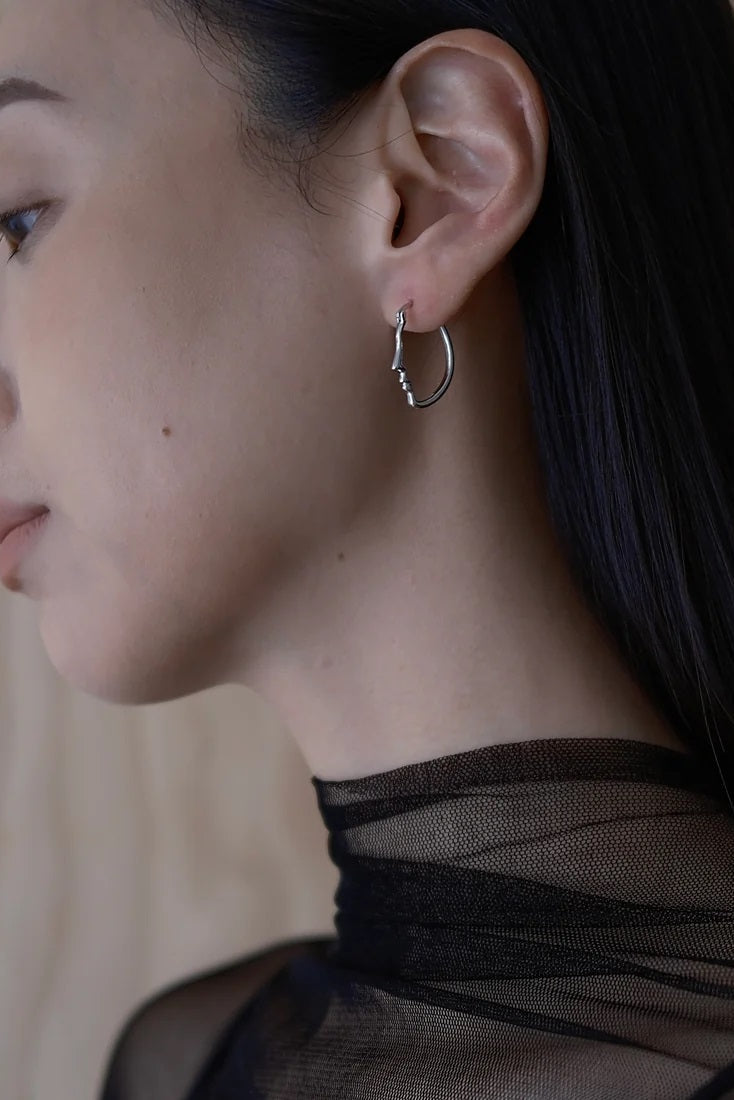 Close-up of a person wearing a silver hoop earring with a neutral background
