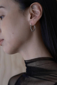 Close-up of a person wearing a silver hoop earring with a neutral background