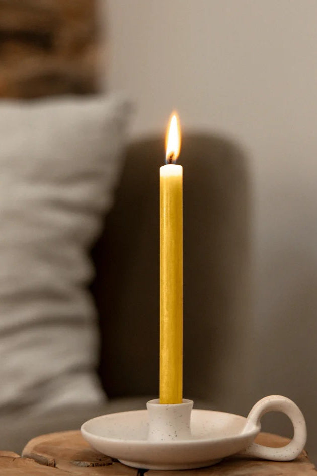 Yellow candle in a white ceramic holder on a wooden surface with a blurred background