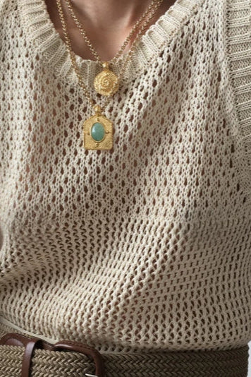 Beige knitted sleeveless top worn by a person with gold necklaces featuring pendants.