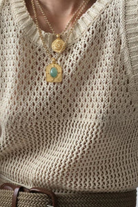 Beige knitted sleeveless top worn by a person with gold necklaces featuring pendants.