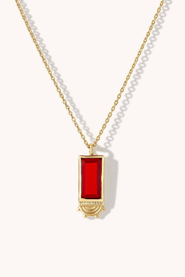 A gold chain necklace featuring a rectangular red gemstone pendant with a gold crescent moon design at the bottom, displayed on a clean off-white background.