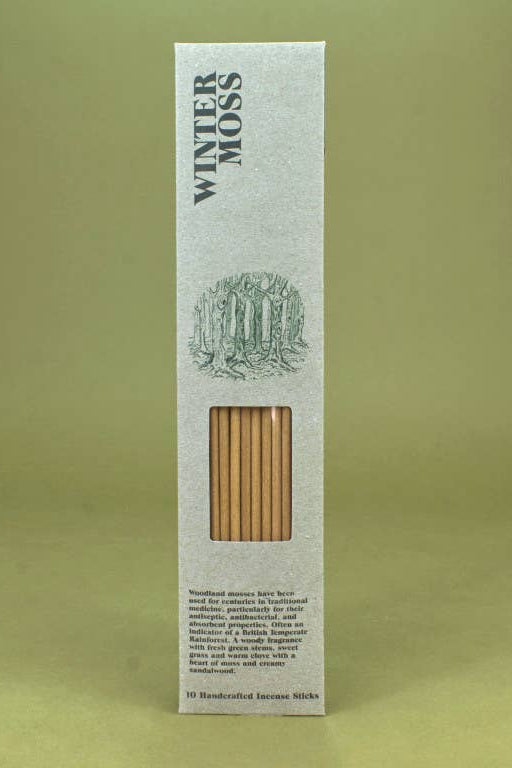A tall, narrow white cardboard box for Winter Moss incense sticks, featuring a green forest illustration and a clear window showing the light brown incense sticks inside, set against a solid olive green background.
