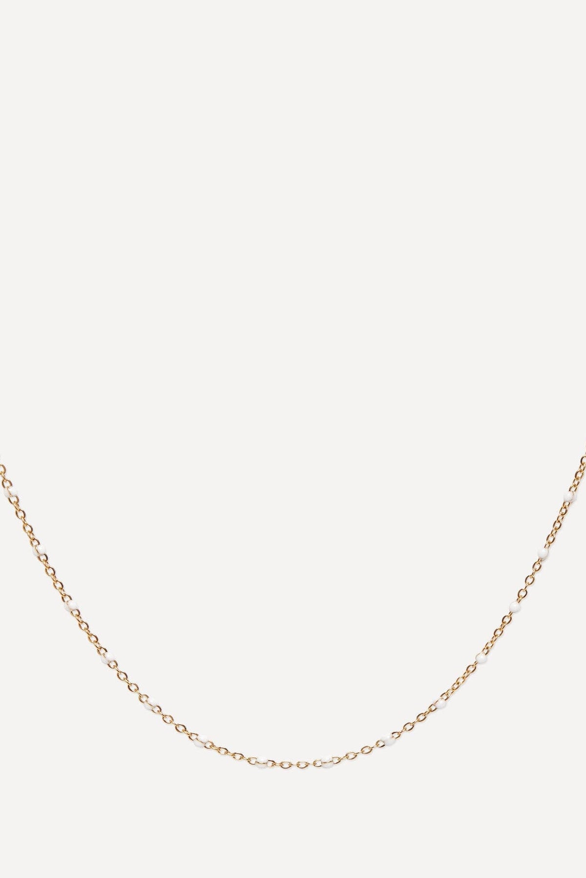 A delicate yellow gold chain necklace with small, closely spaced links, displayed in a curved shape against a solid off-white background.
