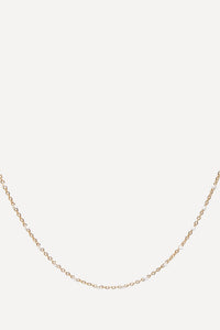 A delicate yellow gold chain necklace with small, closely spaced links, displayed in a curved shape against a solid off-white background.