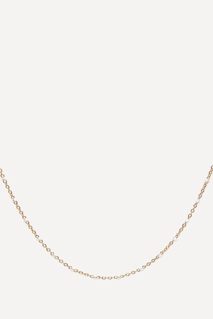 A delicate yellow gold chain necklace with small, closely spaced links, displayed in a curved shape against a solid off-white background.