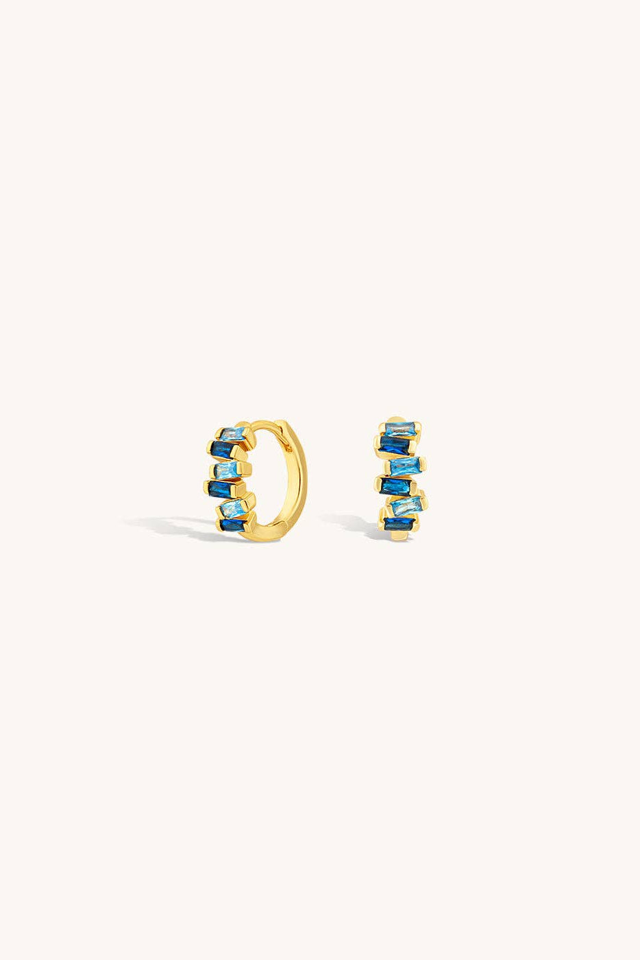 Gold hoop earrings with blue gemstones on a white background