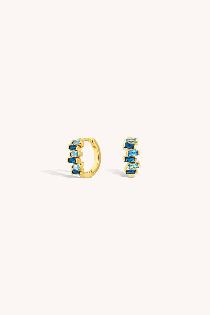 Gold hoop earrings with blue gemstones on a white background