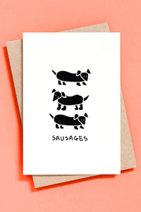 Greeting card with black illustrations of sausage dogs on a white background, placed on a pink surface.