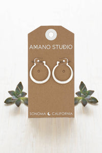 Pair of silver hoop earrings on a 'Amano Studio' branded card with succulents in the background.