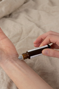 Person applying essential oil to wrist with a dropper bottle on a beige fabric background