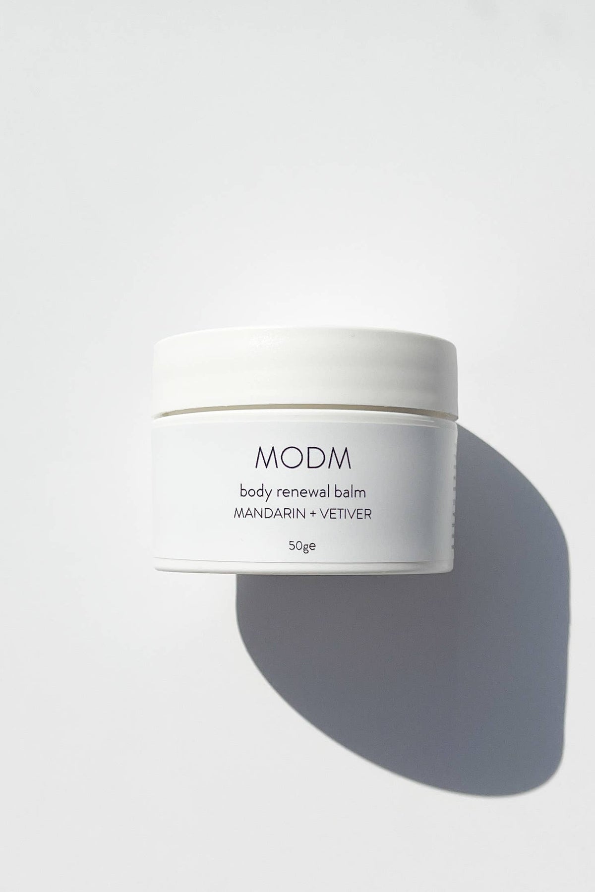 White jar of MODM body renewal balm on a light gray background