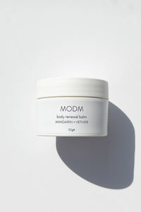 White jar of MODM body renewal balm on a light gray background