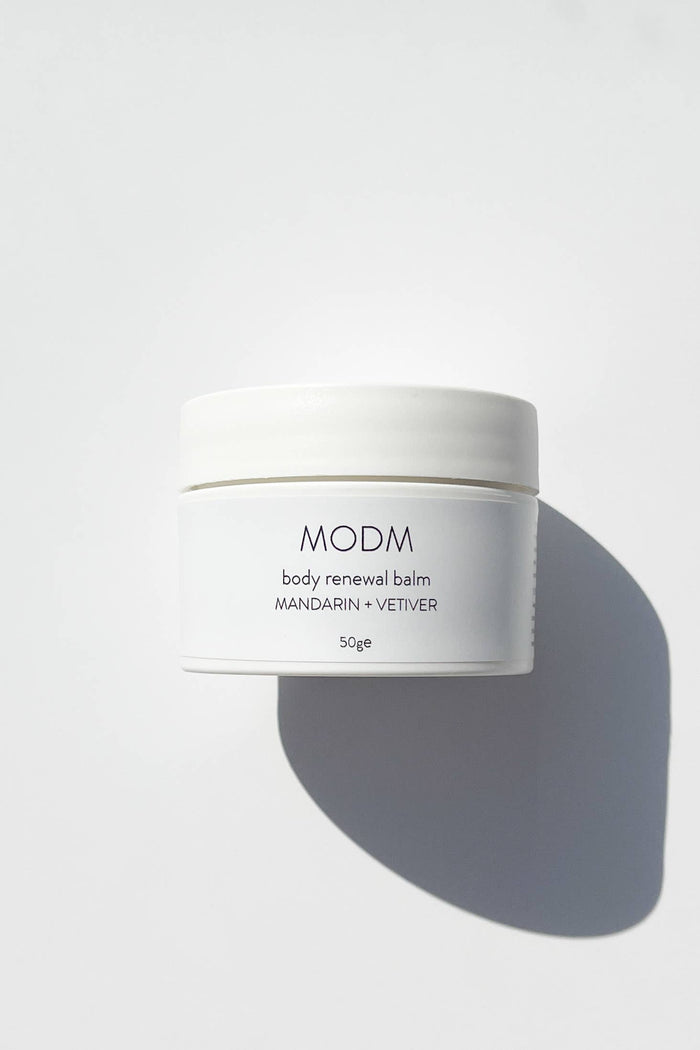 White jar of MODM body renewal balm on a light gray background