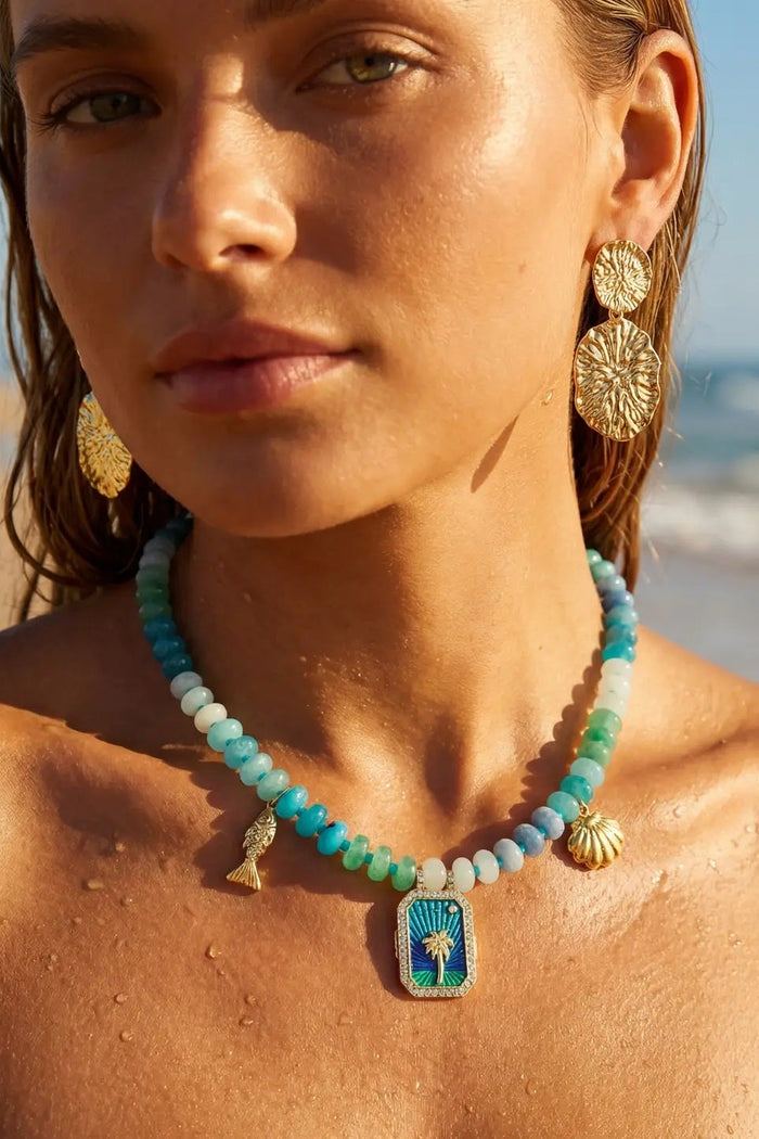 Woman on a beach wearing a turquoise beaded necklace with a pendant.