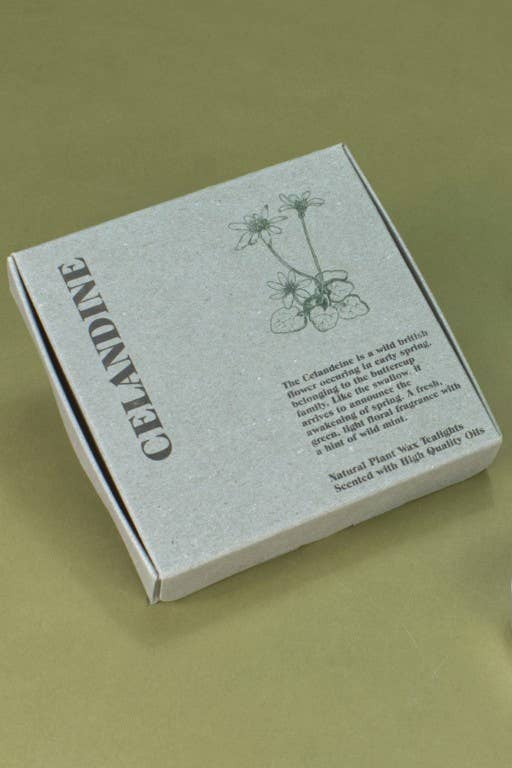 Three small white tea light candles arranged next to a square gray box printed with botanical illustrations and the word 'Celandine' on a muted olive background.