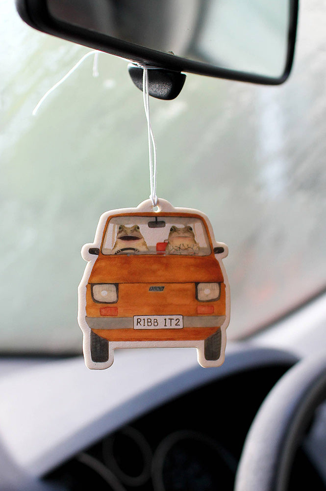 Car air freshener shaped like a vintage orange car with cartoon dogs inside, hanging from a car's rearview mirror.